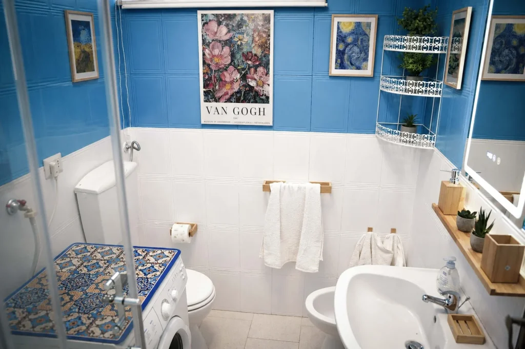 Bagno principale con lavatrice, sanitari e pareti azzurre decorato con quadri di Van Gogh presso la casa vacanze a Cariati.