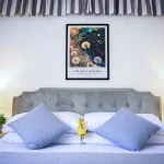 Letto matrimoniale con testata in velluto grigio, cuscini azzurri e quadri botanici alla Dimora di Arianna a Cariati.