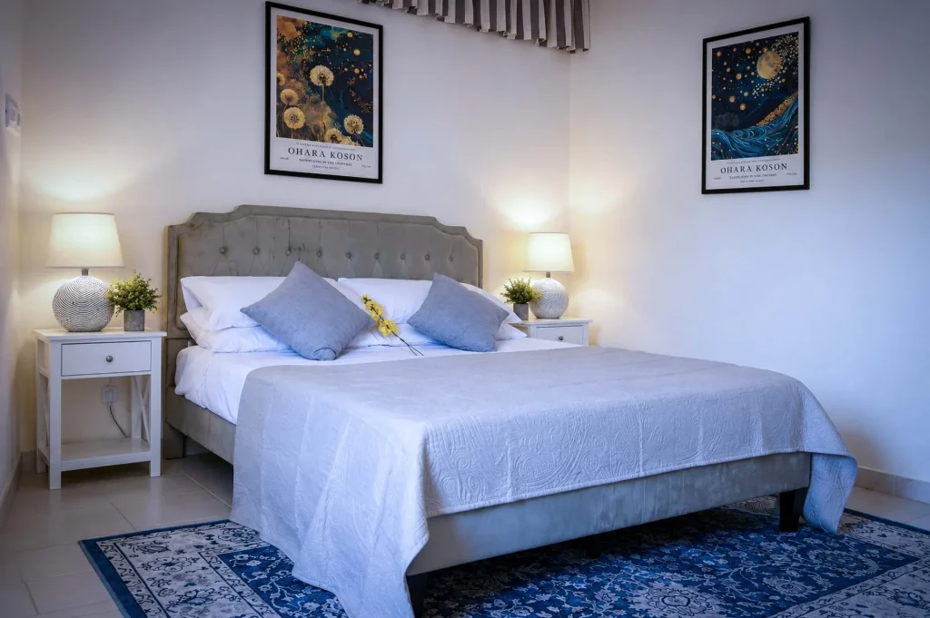 Letto matrimoniale con testata grigia, cuscini azzurri, quadri di Ohara Koson e lampade da comodino accese alla Dimora di Arianna a Cariati.