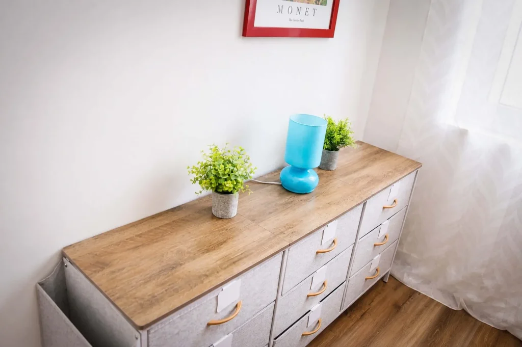 Cassettiera moderna in legno chiaro e tessuto con lampada azzurra e piantine decorative nella cameretta della casa vacanze a Cariati.
