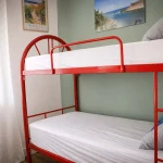 Letto a castello in metallo rosso con cuscini grigi e blu davanti a una parete verde salvia nella casa vacanze La Dimora di Arianna.
