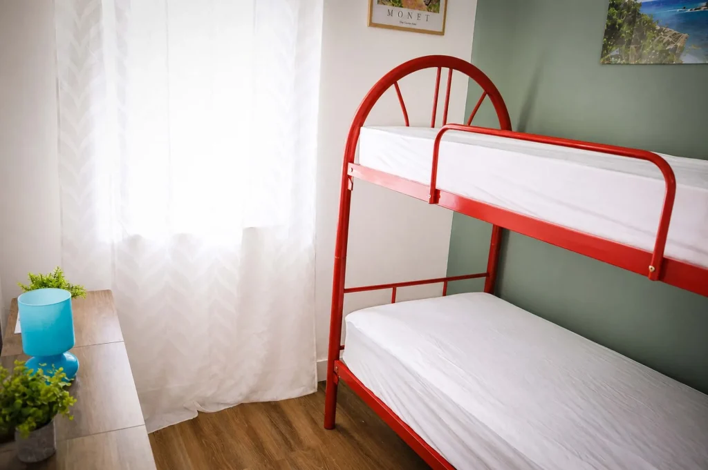 Cameretta con letto a castello rosso in metallo, cassettiera, lampada azzurra e finestra luminosa a Cariati Marina.
