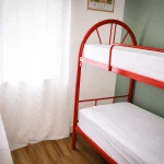 Cameretta con letto a castello rosso in metallo, cassettiera, lampada azzurra e finestra luminosa a Cariati Marina.