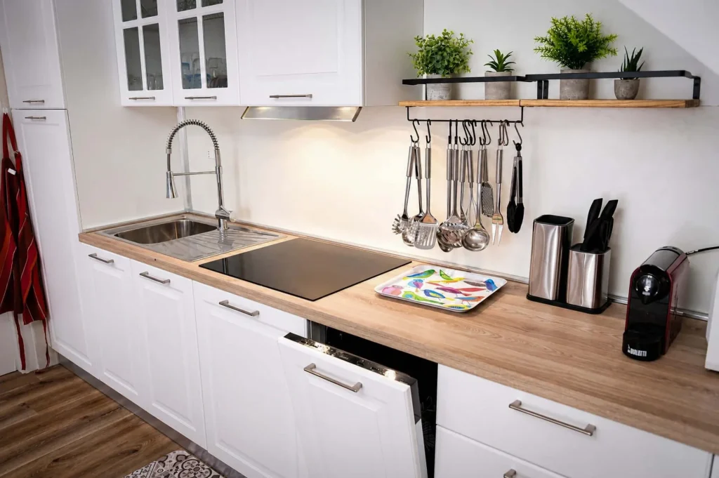 Dettaglio del piano di lavoro in legno della cucina con utensili appesi, lavastoviglie aperta e macchina del caffè espresso a Cariati.