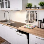 Dettaglio del piano di lavoro in legno della cucina con utensili appesi, lavastoviglie aperta e macchina del caffè espresso a Cariati.