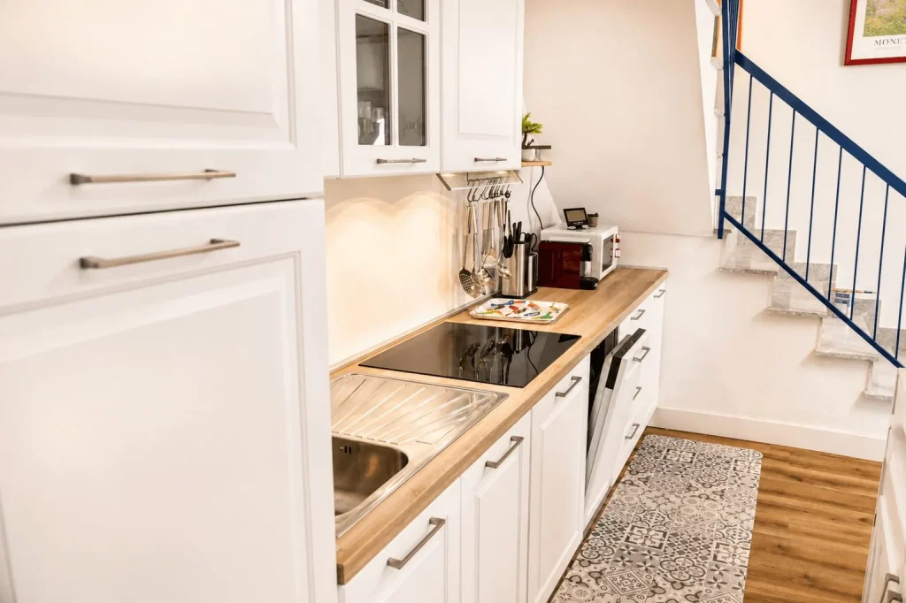 Prospettiva laterale della cucina bianca e della scala interna con ringhiera blu nella casa vacanze La Dimora di Arianna a Cariati.
