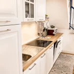 Prospettiva laterale della cucina bianca e della scala interna con ringhiera blu nella casa vacanze La Dimora di Arianna a Cariati.