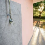 Doccia esterna con soffione cromato e parete rivestita in pietra grigia nel giardino della casa vacanze La Dimora di Arianna.