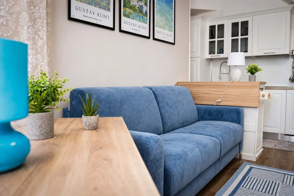 Soggiorno moderno con divano azzurro, tavolino in legno chiaro, lampada turchese e scorcio della cucina a Cariati Marina.