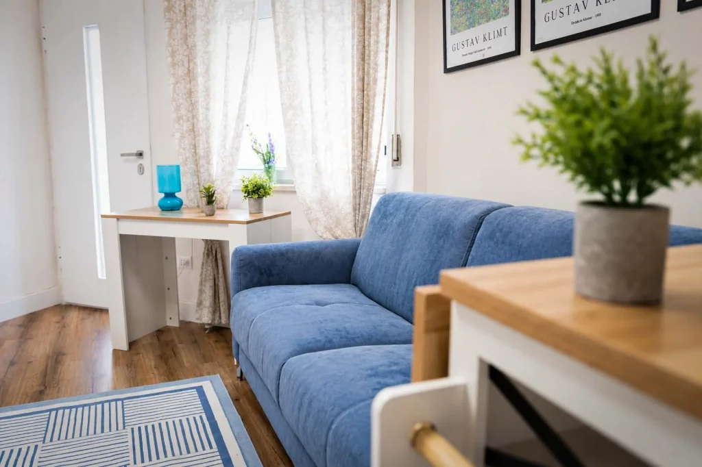 Salone open space della casa vacanze con divano letto azzurro, scrivania bianca con lampada turchese e tende decorate a Cariati.