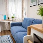 Salone open space della casa vacanze con divano letto azzurro, scrivania bianca con lampada turchese e tende decorate a Cariati.
