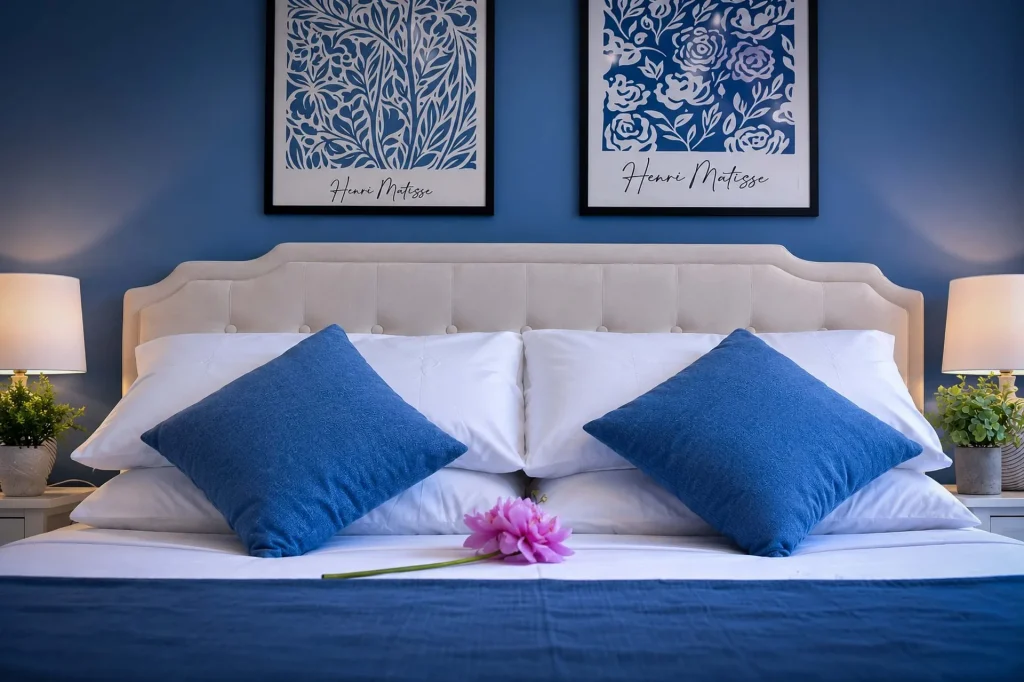 Letto matrimoniale con testata beige, cuscini blu cobalto e quadri di Henri Matisse su parete blu alla Dimora di Arianna a Cariati.