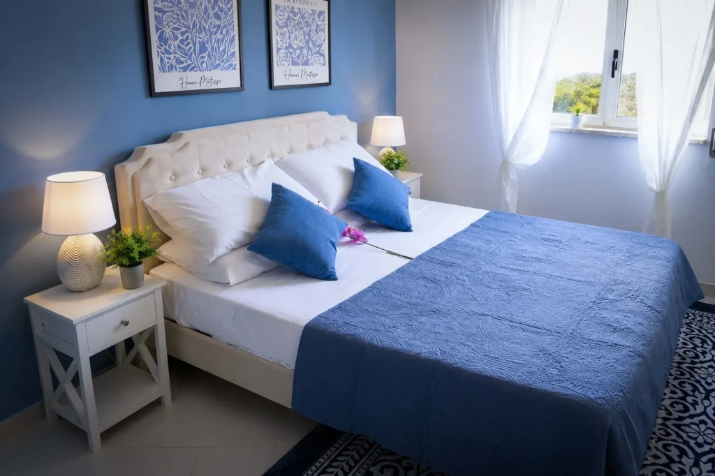 Seconda camera da letto completa con letto matrimoniale, comodini bianchi, pavimento in gres e finestra con tende bianche a Cariati.