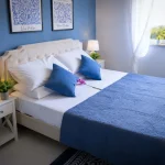 Seconda camera da letto completa con letto matrimoniale, comodini bianchi, pavimento in gres e finestra con tende bianche a Cariati.