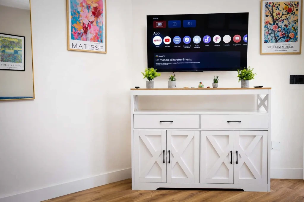Smart TV a schermo piatto appesa alla parete sopra una credenza in legno bianco con decorazioni floreali a Cariati Marina.