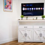 Smart TV a schermo piatto appesa alla parete sopra una credenza in legno bianco con decorazioni floreali a Cariati Marina.