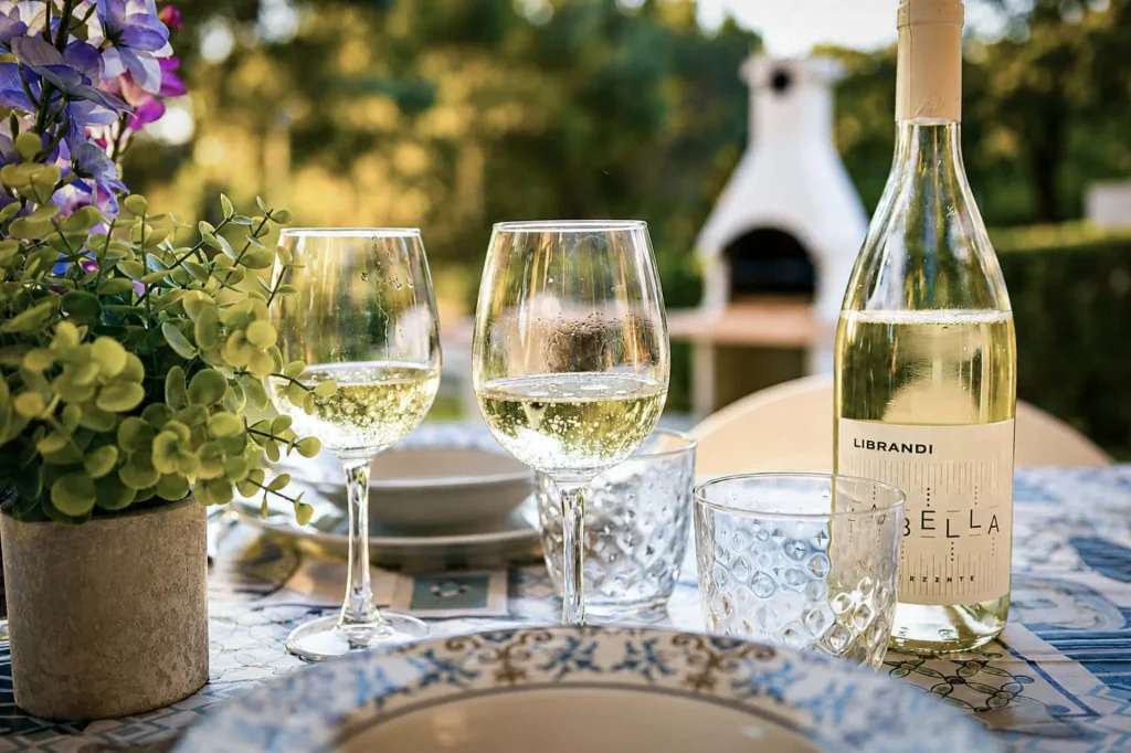 Due calici di vino bianco frizzante e una bottiglia di vino Librandi su una tavola apparecchiata nel giardino a Cariati Marina.
