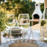 Due calici di vino bianco frizzante e una bottiglia di vino Librandi su una tavola apparecchiata nel giardino a Cariati Marina.