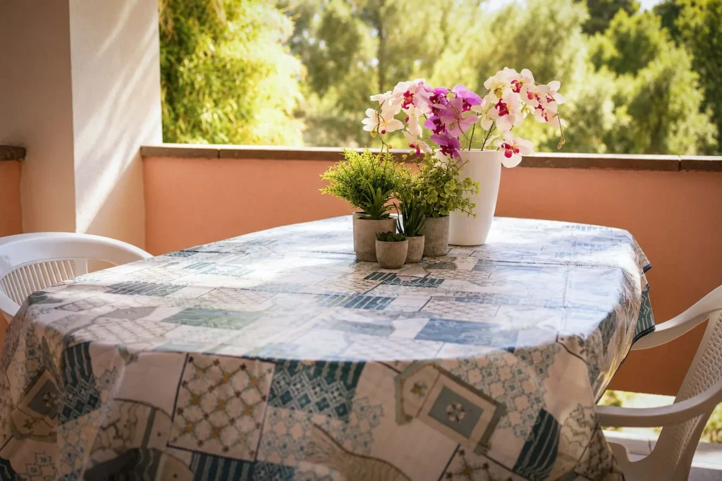 Tavolo da pranzo allestito con tovaglia azzurra e sedie bianche sulla terrazza coperta circondata dal verde a Cariati Marina.