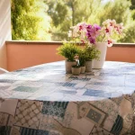 Tavolo da pranzo allestito con tovaglia azzurra e sedie bianche sulla terrazza coperta circondata dal verde a Cariati Marina.
